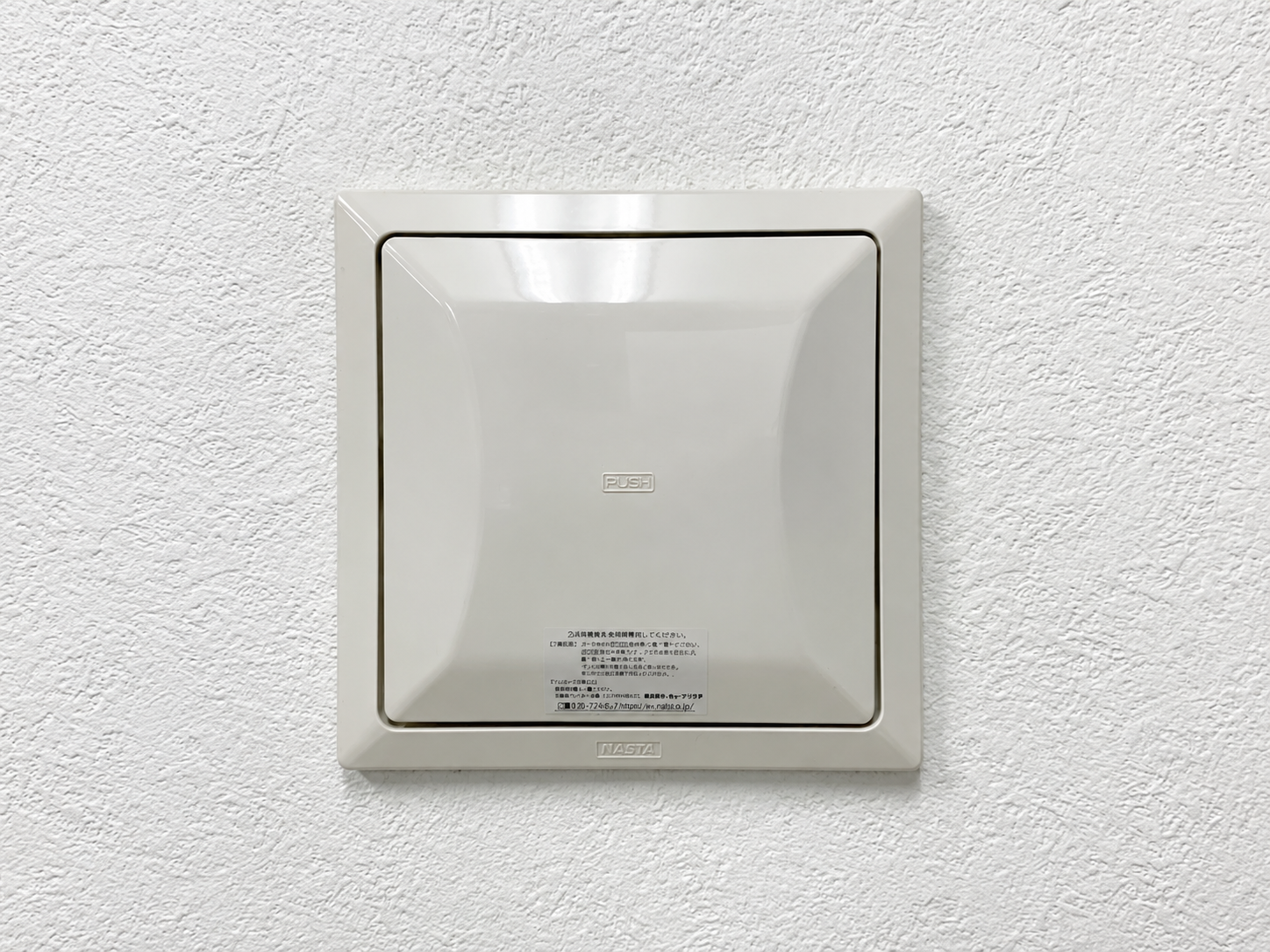 KS-8640PRの取り付け先換気口。白い壁紙に取り付けられた閉じたグリルの正面写真。